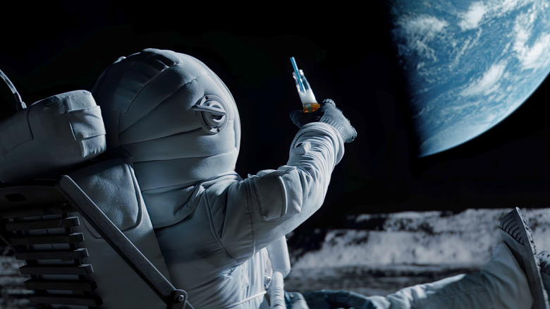 An astronaut lounging on the Moon salutes the Earth by holding up a bottle with a straw inside