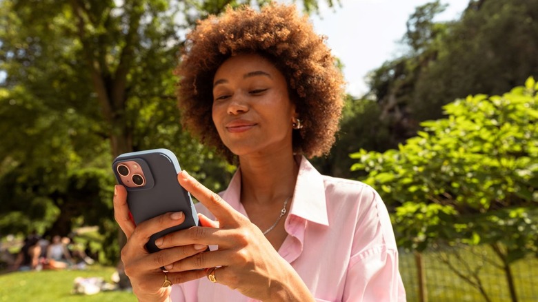 Woman smiling at the park as she looks at her phone