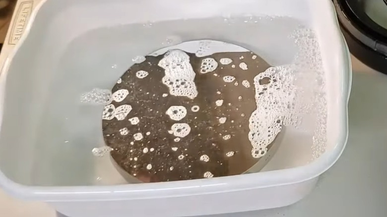 A telescope mirror in a container of soapy water.