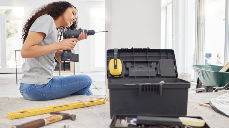 Woman using a power drill with a toolbox in the foreground