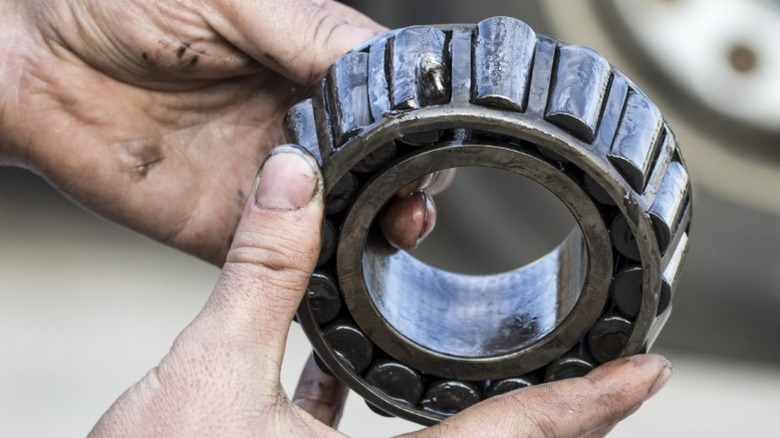 A closeup of a person holding a worn out old-style cone-shaped wheel bearing with visible damage