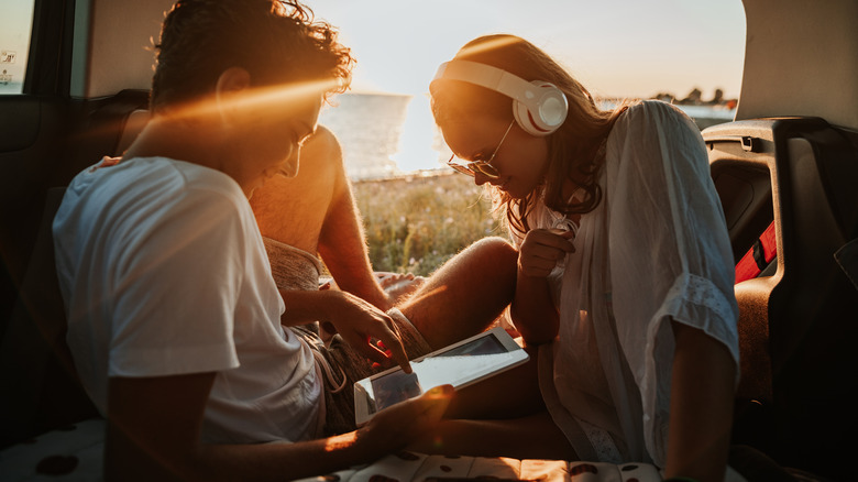 A young couple in the back of a vehicle enjoying some technology while camping.