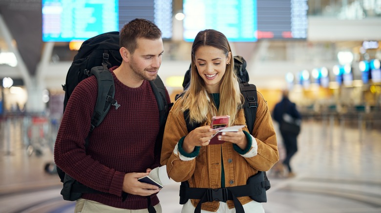 A couple with backpacks at the airport looking at a smartphone.