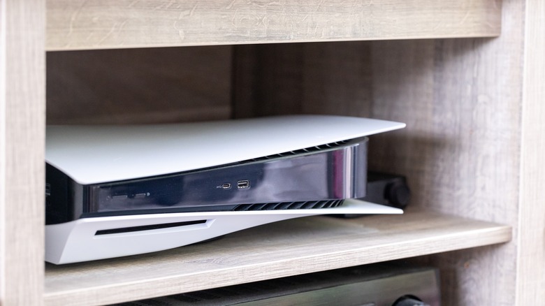 A PS5 console sitting on a wooden entertainment center shelf