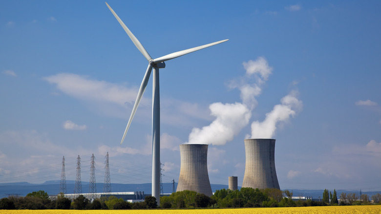 Nuclear power plants with vapor coming out of the smokestacks behind a wind turbine