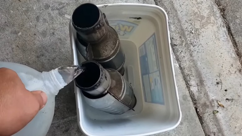 A person pouring vinegar into a bucket with two catalytic converters