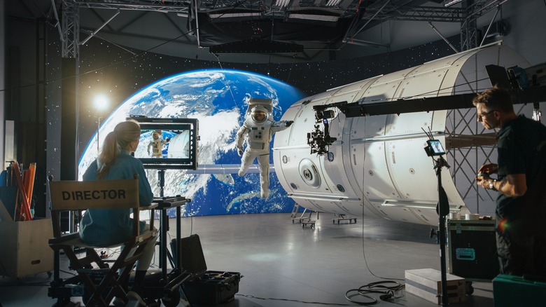 A sci-fi movie set featuring an astronaut, a space shuttle, a female director, and Earth brightly lit up in the background.