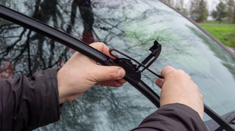 A pair of hands hold a car's windshield wiper while replacing it