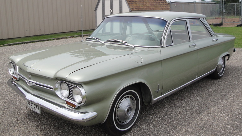 A green 1964 Chevrolet Corvair Monza parked in a driveway in front of fence and shed