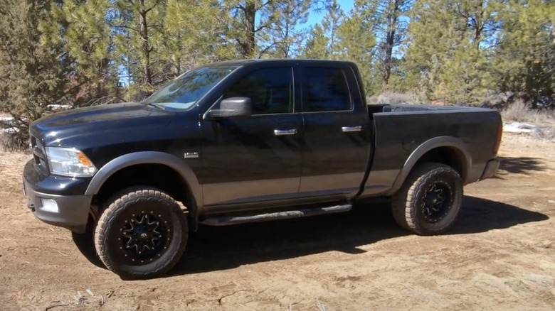 Black fourth-generation Ram pickup parked in dirt in clearing in woods