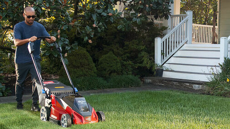 Man in jeans and blue t-shirt mowing lawn with Toro mower