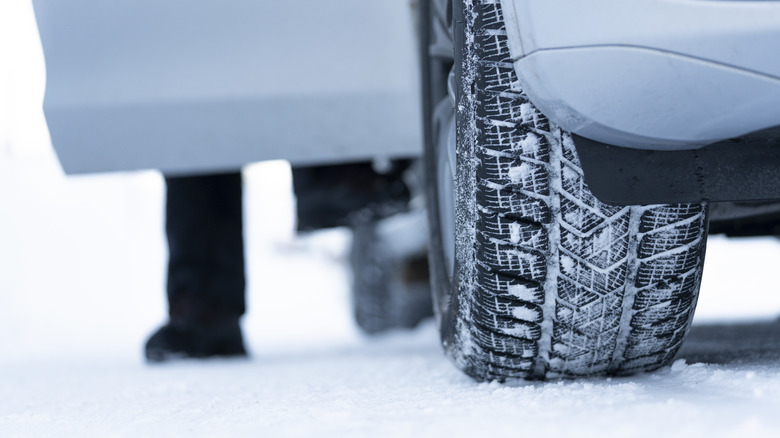 Close-up of snow-covered winter tires with a man getting out of a car on a snowy road.