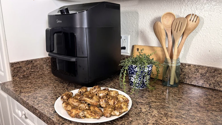 The Midea Two-Zone Air Fryer Oven on a kitchen counter with a plate of yummy chicken wings