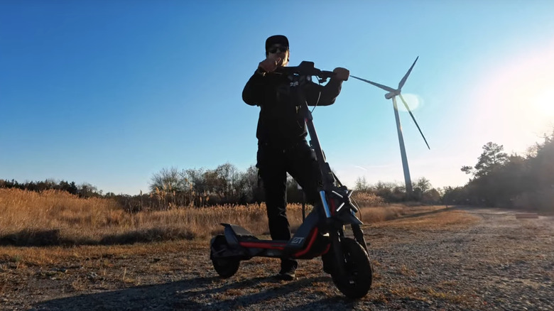 man walking Segway ZT3 scooter on dirt road with windmill in background