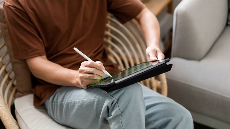 Man sitting in a chair taking notes on an iPad with a stylus