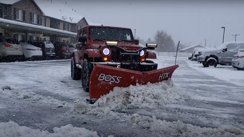 A red Jeep Wrangler plows snow in a parking lot