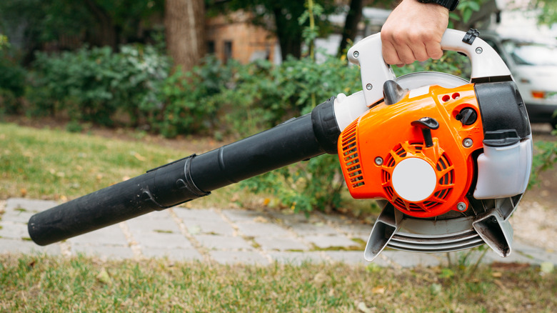 Hand holding an orange and white leaf blower in a yard