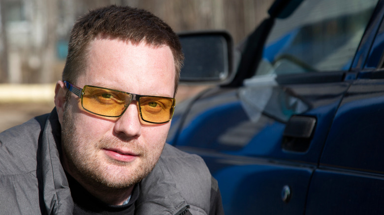 Caucasian man beside a blue car wearing polarized yellow glasses for driving a car