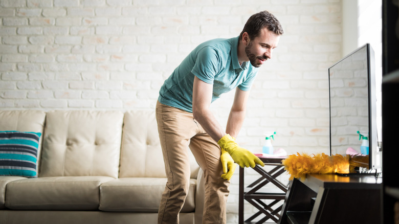 Man using duster to clean around  flat-sceen TV