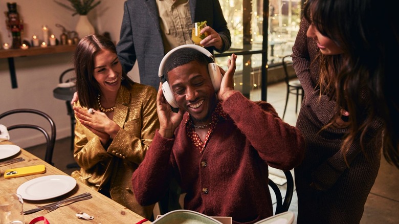 Smiling people gather around a man trying on headphones