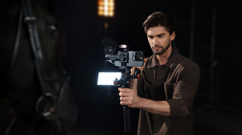 Bearded man in brown shirt using the Hohem iSteady M7 smartphone gimbal in a dark room