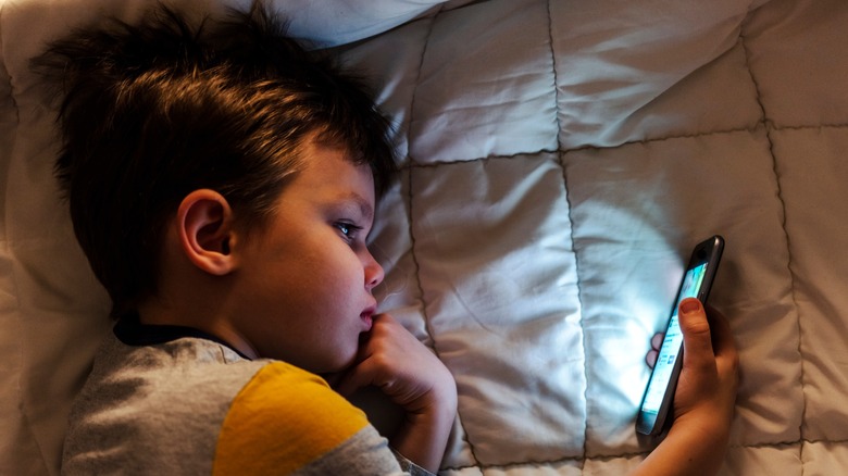 Kid looking at phone in bed 