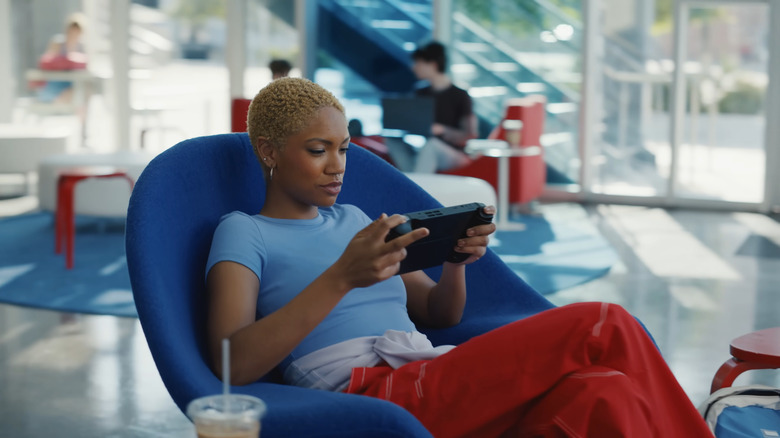 Woman gaming on handheld console while sitting in blue chair