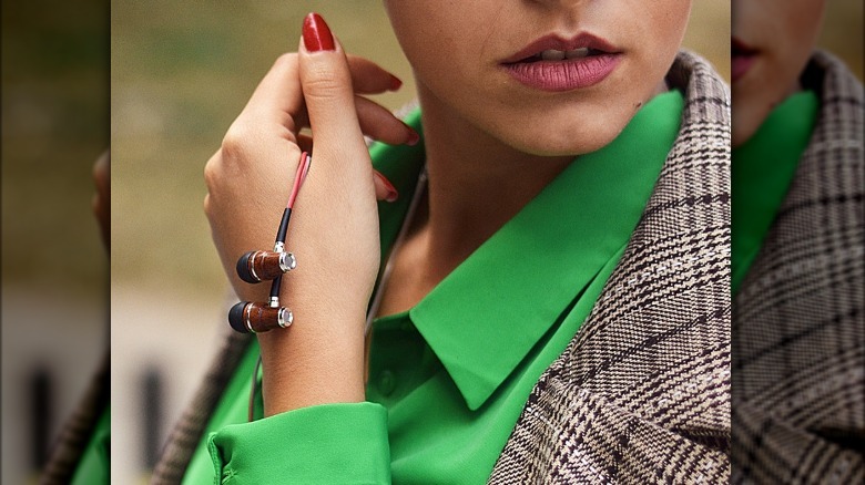 Woman wearing green silk blouse and tweed blazer holding a pair of Symphonized wooden earbuds